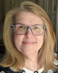 A White woman with blond shoulder-length hair and large dark brown glasses