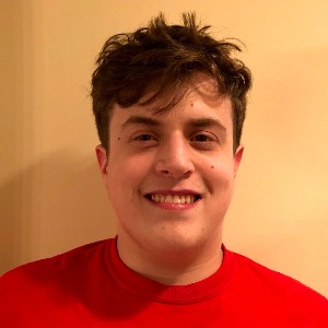 Head-and-shoulders portrait of a smiling young man with fair skin and tousled dark hair, wearing a red shirt