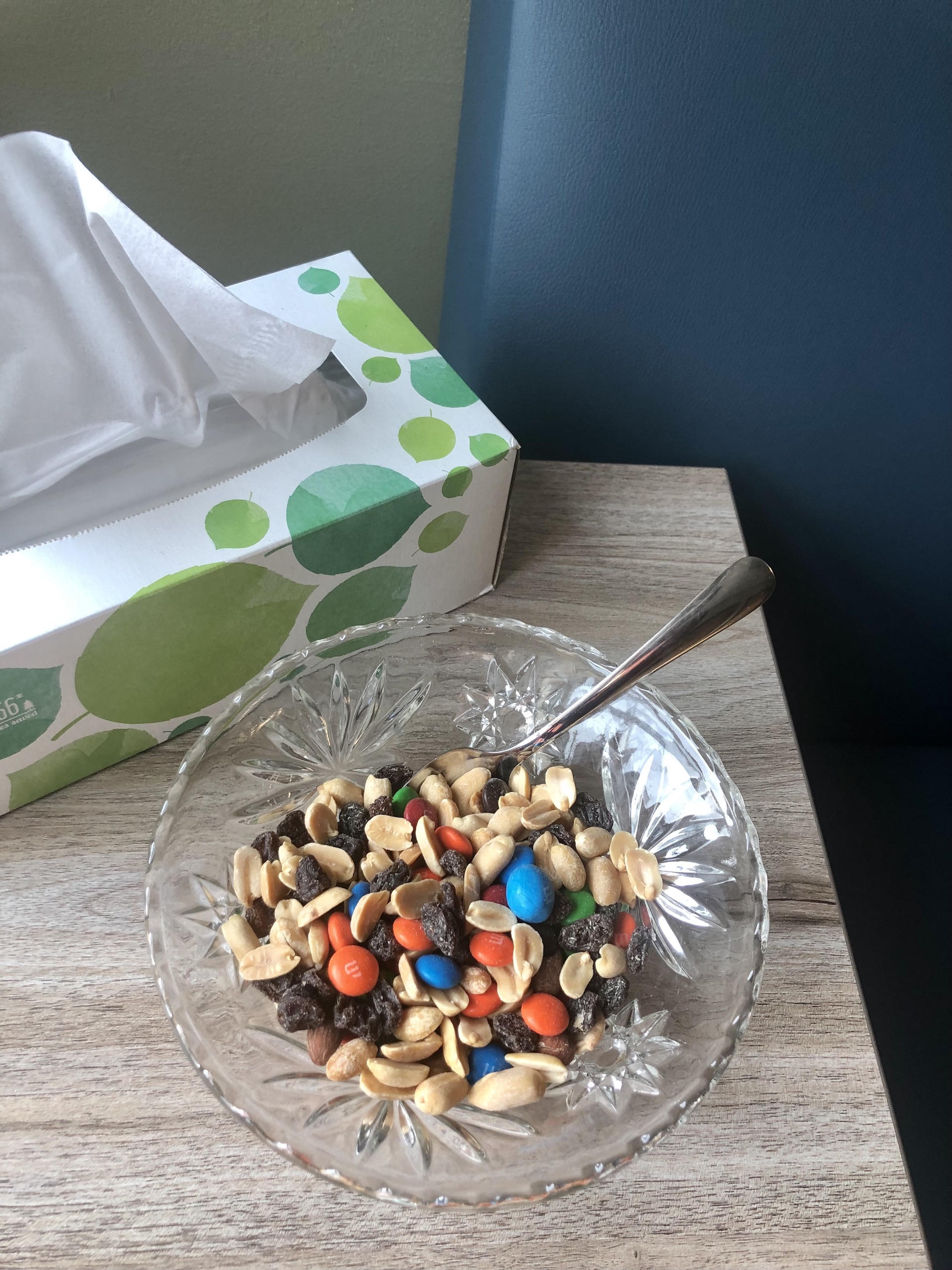 A glass bowl of trail mix with peanuts, raisins, and M&Ms