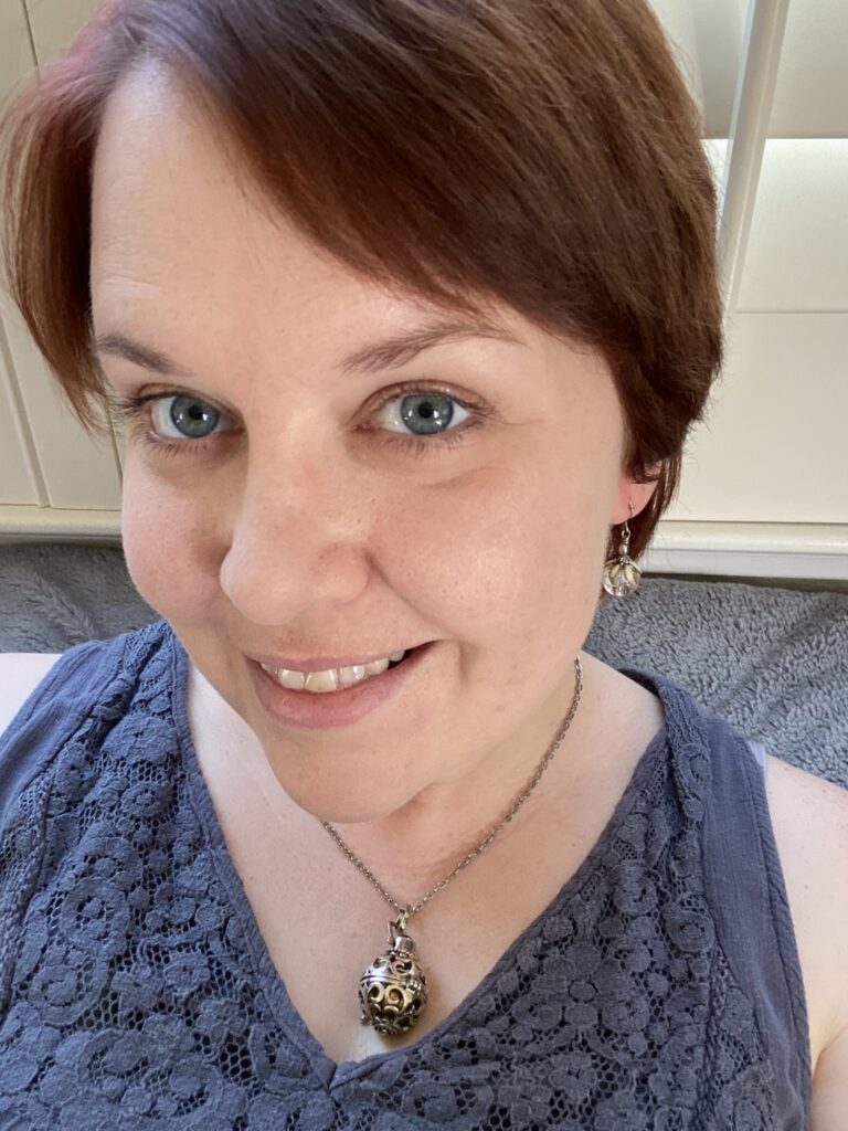 Head shot of a smiling woman with fair skin, auburn hair, and blue eyes, wearing a purple top and silver necklace