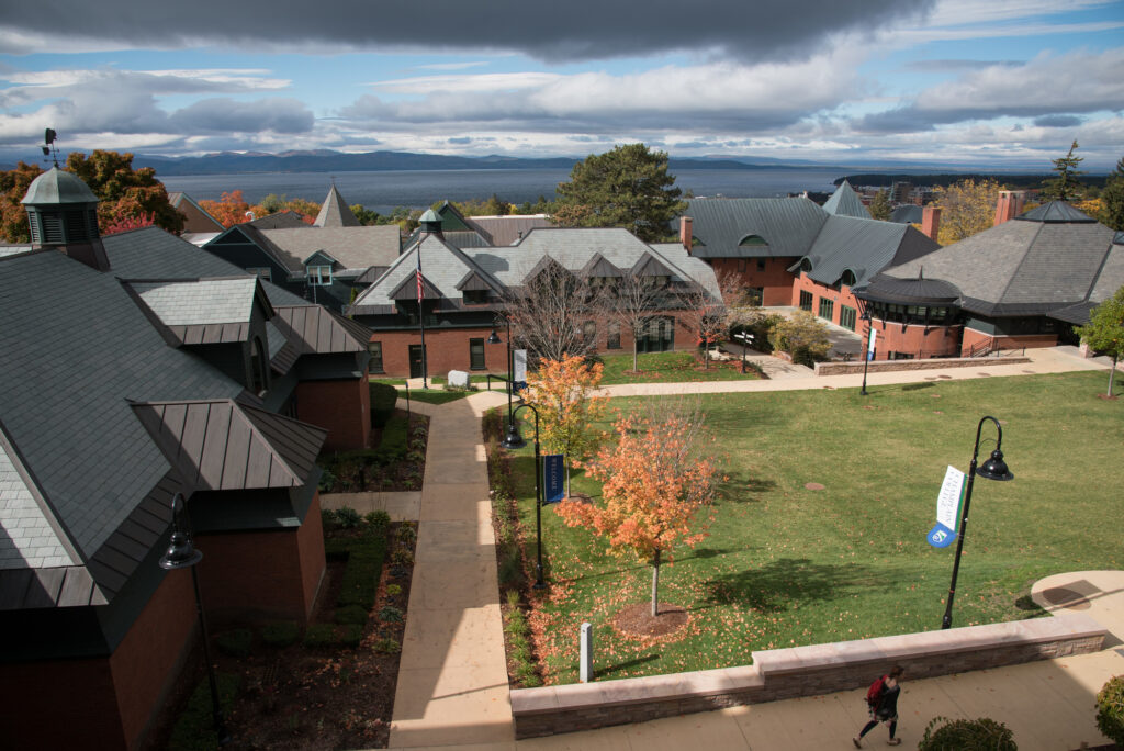 A college campus with a grassy lawn in the foreground and brick buildings behind.